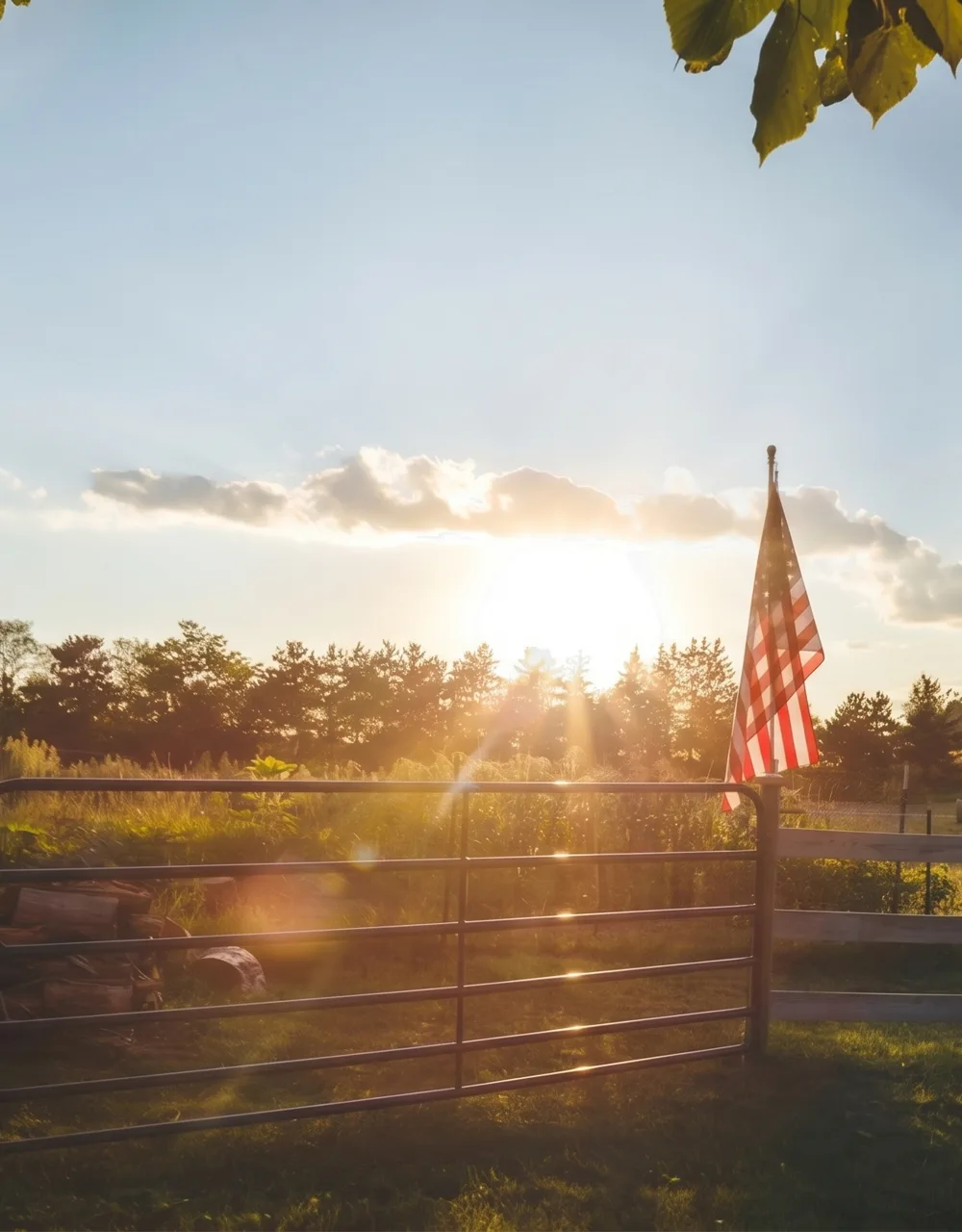 An American flag flying over a rural farm at sunset